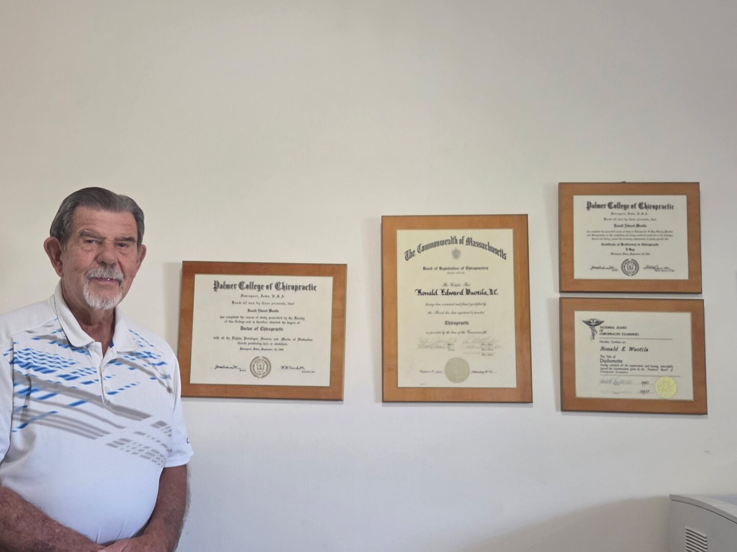 Dr. Wuotila standing beside four framed certificates in his office.